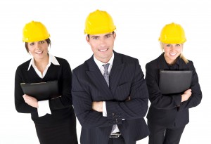 An industrial concept shot showing 2 women and a man dressed in hard hats. The focus is on the man in the foreground
